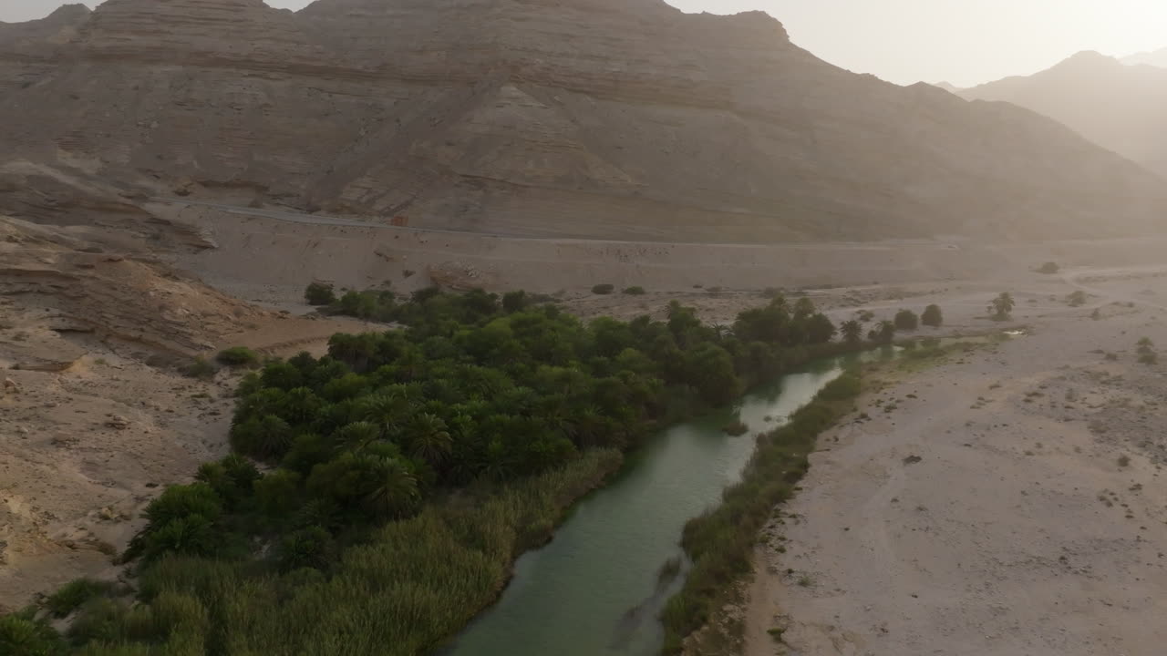 Lush oasis surrounded by arid mountains and a winding stream in Oman