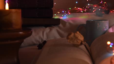 cozy background of an open book on a bed, next to a mug and surrounded by colorful christmas lights