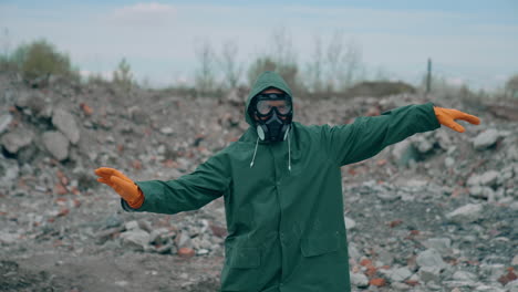 Man in safety suit and respirator on garbage background. Mad man in protective costume and gas mask dancing in abandoned place in radioactive zone.