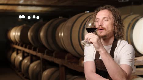 authentic shot of successful male sommelier is tasting a flavor and checking white wine quality poured in transparent glass in a wine cellar.