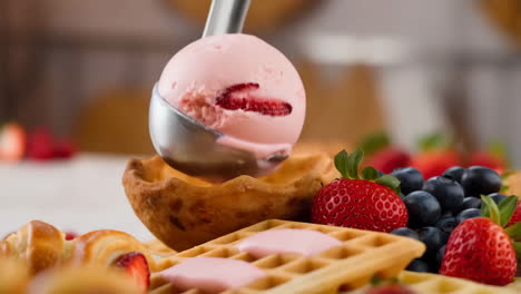scooping strawberry ice cream into a waffle bowl with fresh berries