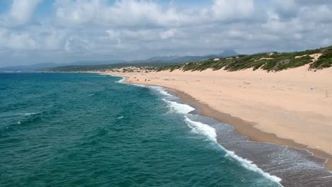 Flying-over-the-sea,-beach-and-sand-dune-in-Sardaigna,-dunes-of-Piscinas