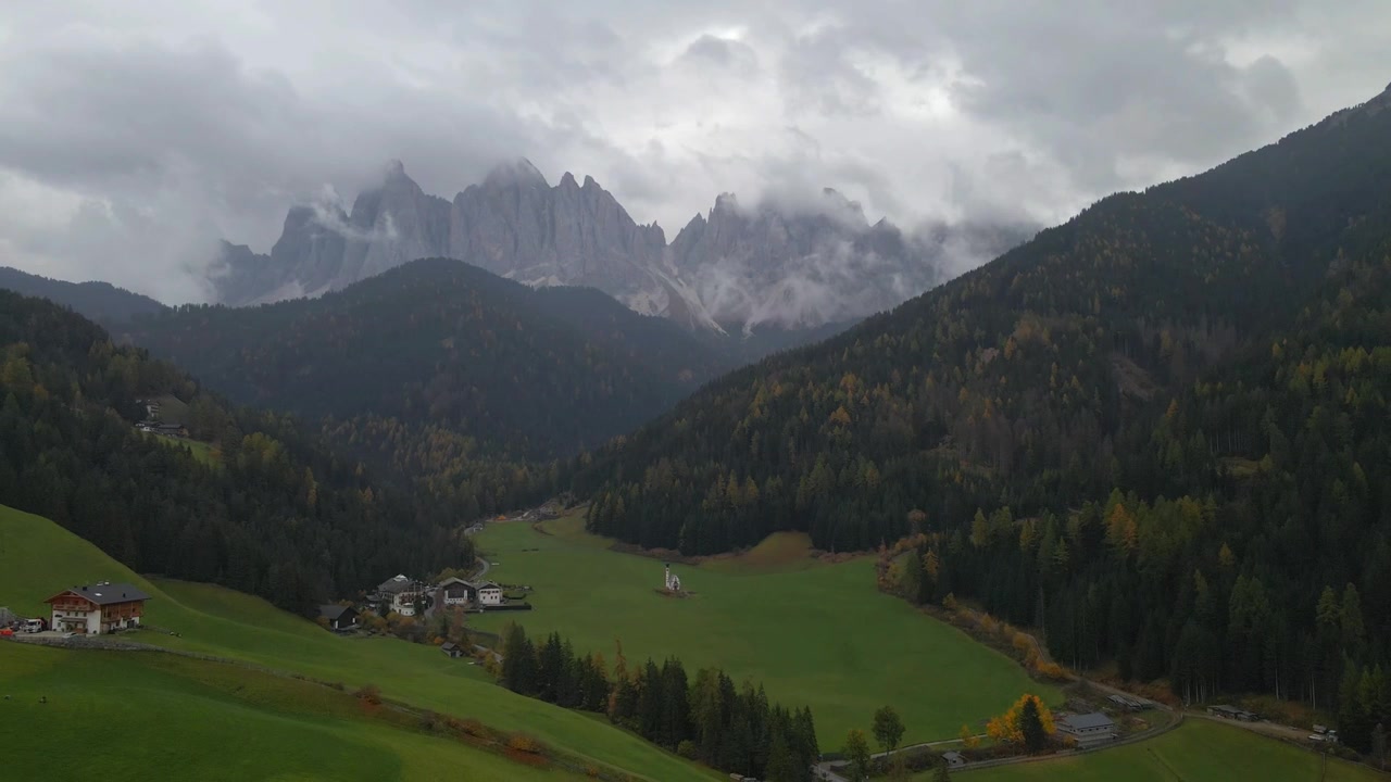 Una vista mozzafiato di Santa Maddalena in Alto Adige, Italia, con lussureggianti valli verdi, case pittoresche e imponenti cime montuose circondate dalla nebbia e dai colori autunnali, che creano un'atmosfera serena.