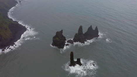 aerial: reynisdrangar sea stacks in reynishjara black sand beach in iceland