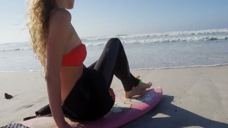 Surfista-Femenina-Relajándose-En-Una-Tabla-De-Surf-En-La-Playa-4k