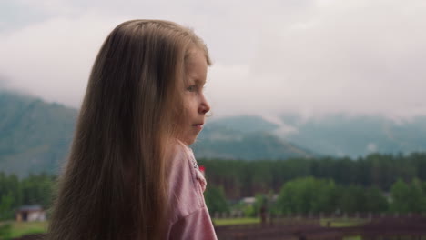 amazed little girl enjoys view of misty mountains at resort