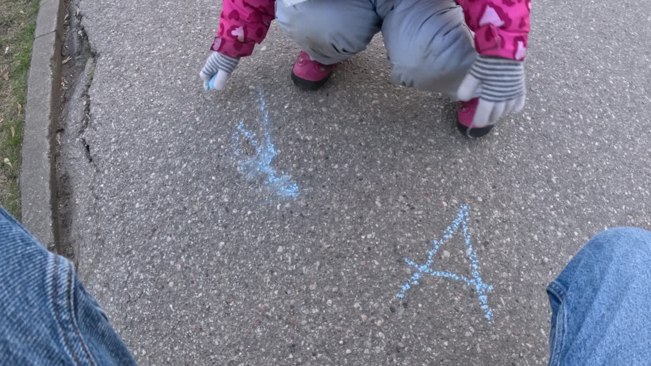Young girl drawing with crayons on asphalt in early spring