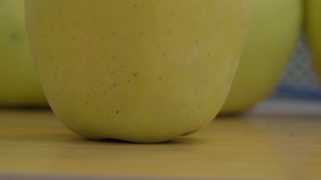 Detailed macro shot capturing the texture of a fresh golden yellow apple on a wooden table, accentuated by soft, natural lighting. Perfect for food, health, or organic lifestyle themes