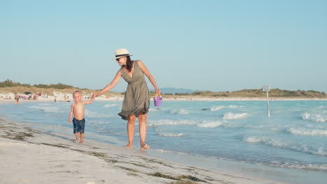 Kleiner-Junge-Springt-Neben-Mutter-Am-Meer.-Frau-Und-Junge-Gehen-Am-Strand-Entlang.