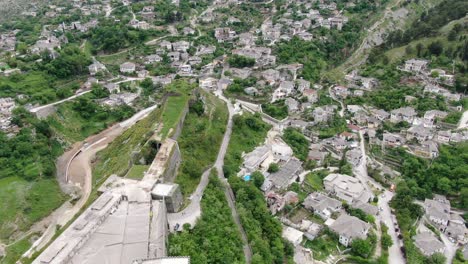 Drone-view-in-Albania-flying-in-Gjirokaster-town-over-a-medieval-castle-on-high-ground-top-view-showing-grey-roof-houses