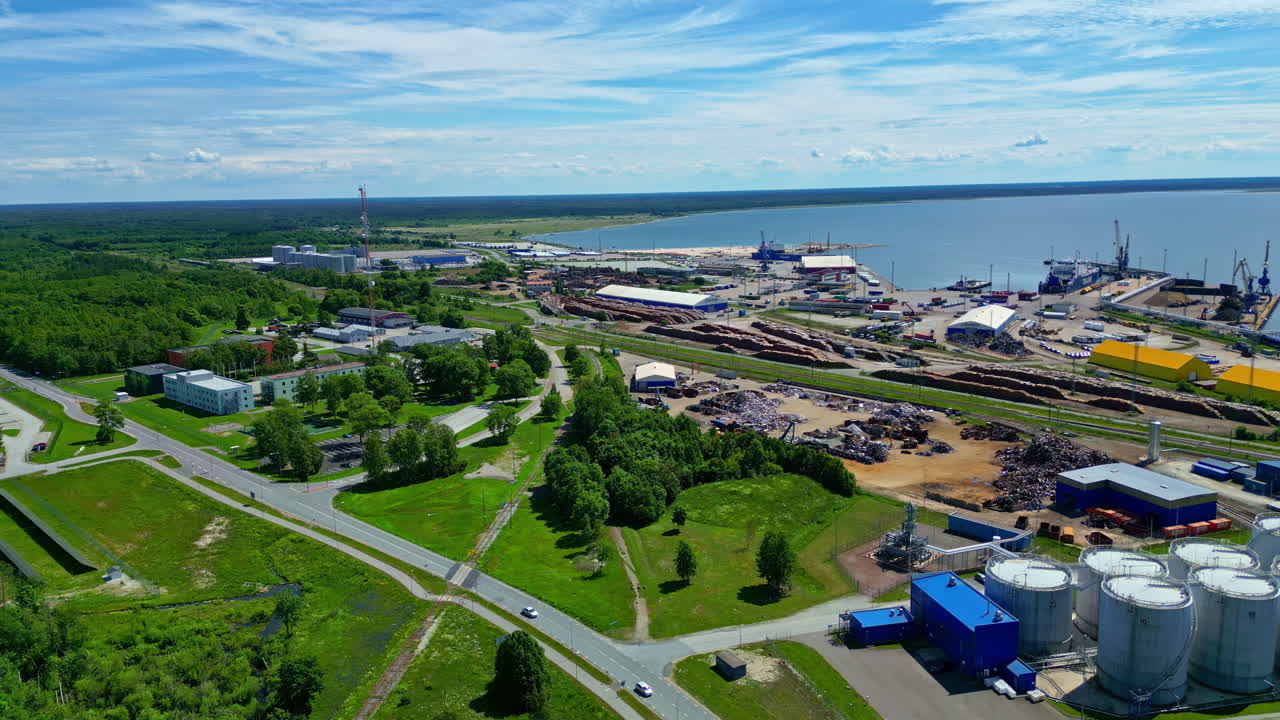 Aerial view of an industrial port with log and scrap metal yards, storage tanks, and buildings