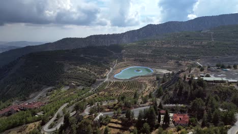 a distant drone view showcases kouris dam, surrounded by a serene landscape of rolling hills, rugged terrain, and tranquil waters blending harmoniously with nature.