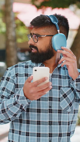 Happy-Indian-man-dancing-in-wireless-headphones-listening-favorite-energetic-music-on-city-street