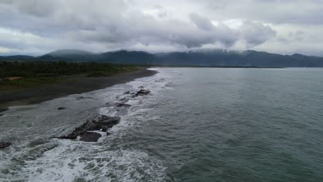 tidal waves crashing against rugged rocks along island coastline during overcast, stormy day at catanduanes, philippines - aerial forward shot