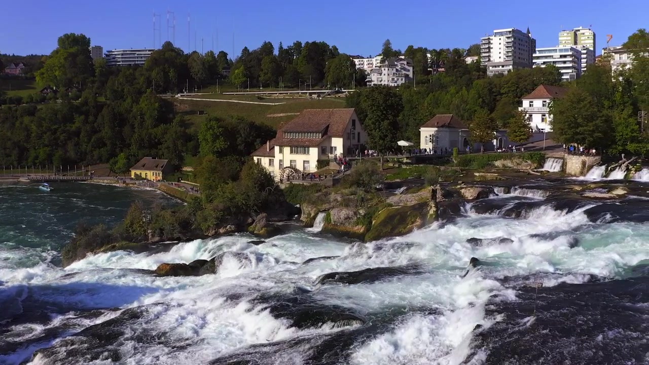 Zeitlupe: Kamerafahrt des tosenden Rheinfalls bei Schaffhausen in der Schweiz. Wassermühle und Menschen im Hintergrund