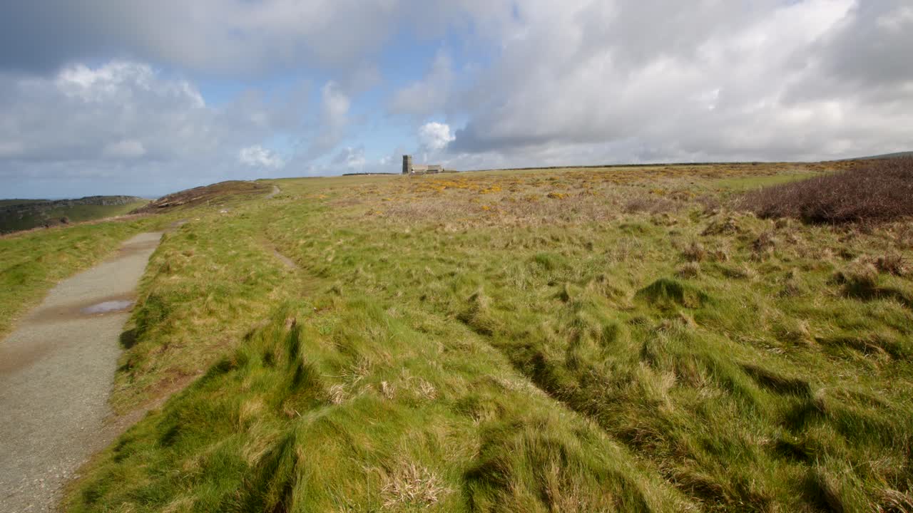 Extra Wide shot of sun lilt coastal path looking at St Materiana's Church, in background, from Lower Penhallic Tregatta