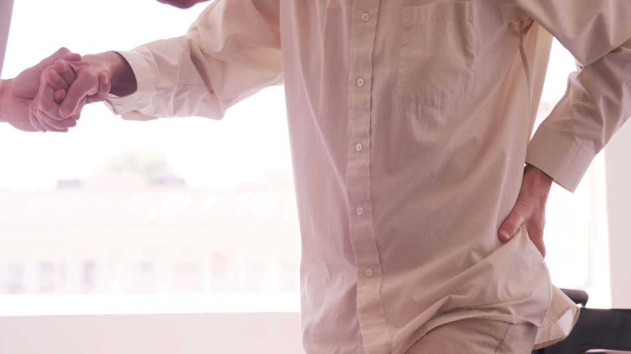 Male doctor assisting senior man to get up from wheelchair
