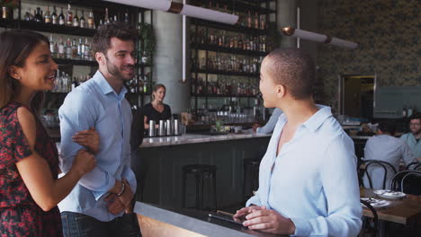 Pareja-Siendo-Recibida-Por-El-Maitre-D-Usando-Una-Tableta-Digital-Cuando-Llegan-Al-Restaurante