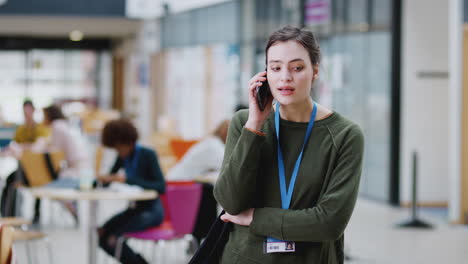 Lächelnde-Studentin,-Die-Im-Belebten-Gemeinschaftsgebäude-Des-Campus-Mit-Dem-Mobiltelefon-Telefoniert