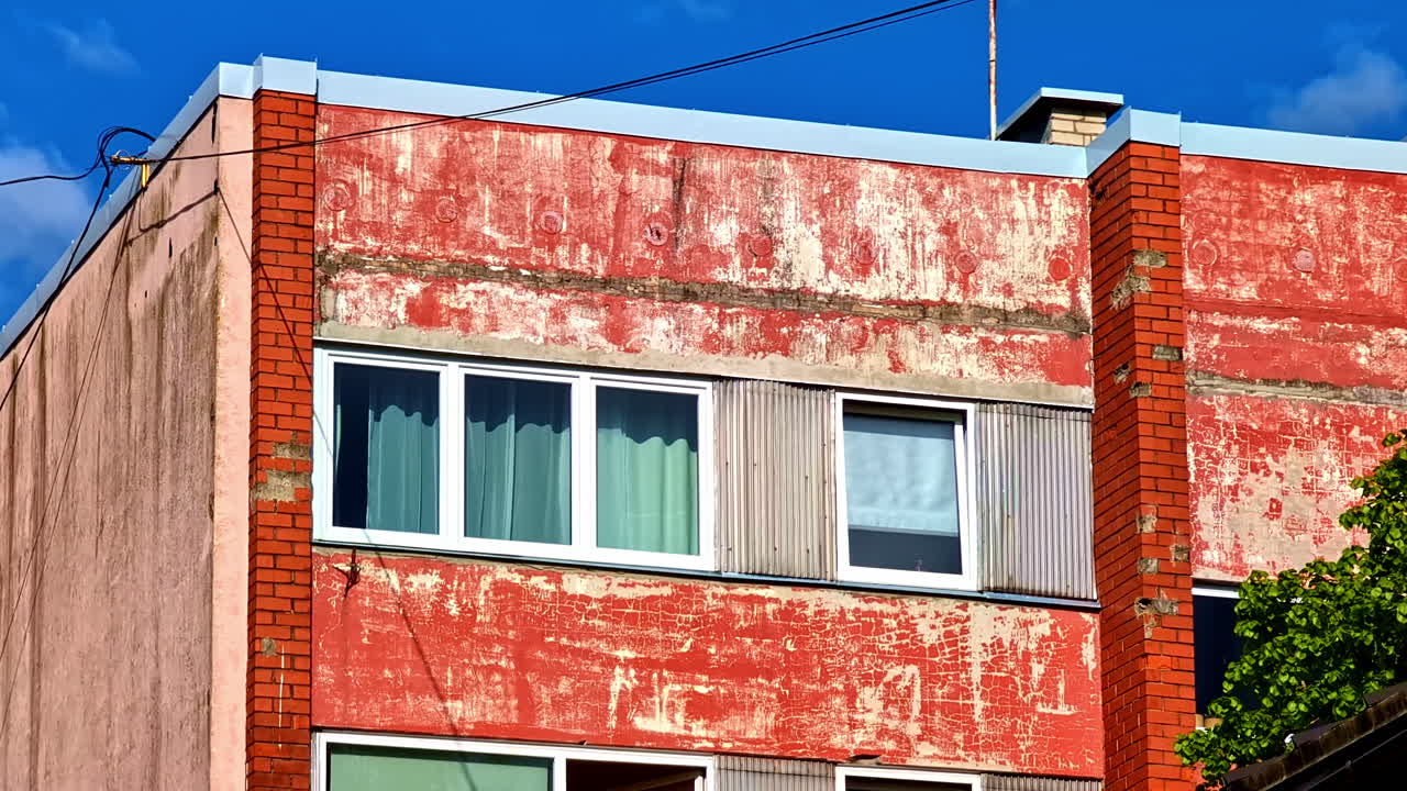 Weathered Red Apartment Building With Exposed Brick Corners and Curtains in Windows