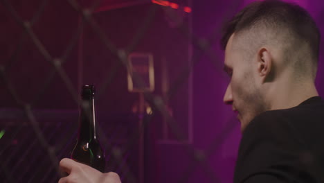 Young-Man-Drinking-Beer-While-Sitting-Alone-At-Disco-Club