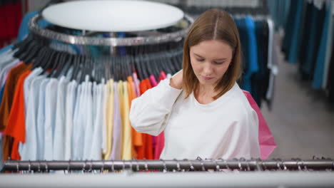 mujer joven navegando a través de coloridos estantes de ropa con una bolsa de compras detrás de ella en una tienda minorista bien iluminada, centrada en la exploración de exhibiciones de ropa moderna con prendas de vestir vibrantes