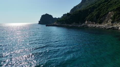 Red-boat-sailing-by-the-lush-coast-of-Corfu-Island-on-a-sunny-day,-clear-blue-Ionic-Sea-waters