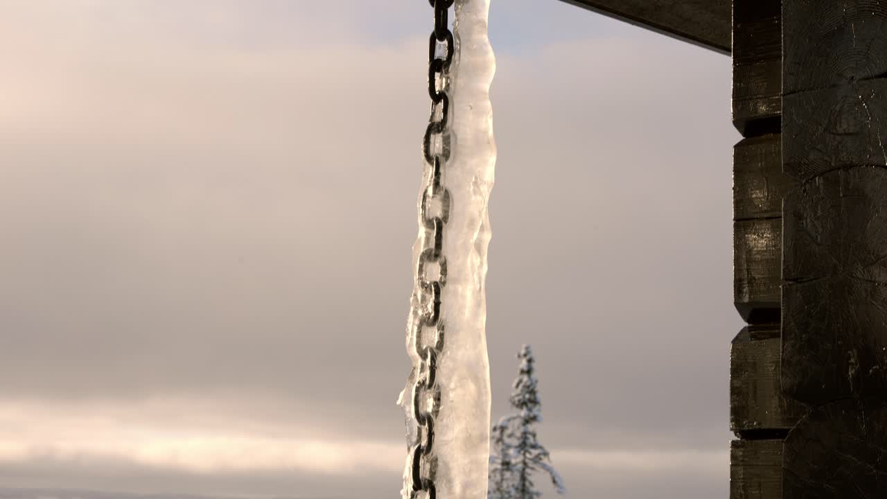 Frossen regnkæde med is mod en gylden solnedgang og en snedækket alpedal, Valdres, Norge.