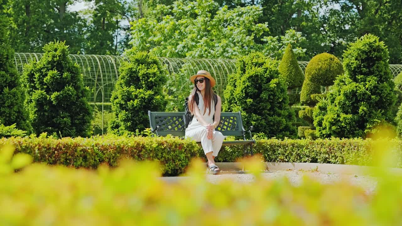 Relaxed lady on bench enjoys quiet charm of sculpted summer park greenery