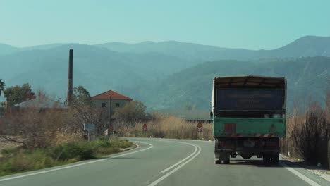 truck driving, scenic countryside road, entering village, pov from behind, mountains