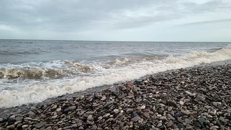 sandy ocean waves crashing slow motion on welsh pebble beach in windy autumn season