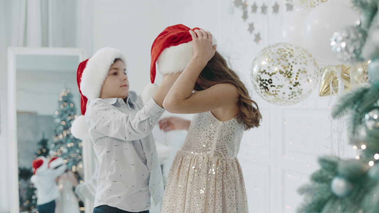 niño serio con sombrero de santa sobre niña en apartamento de año nuevo.