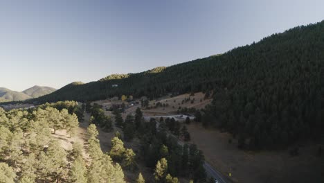 Disparo-De-Un-Dron-Que-Captura-Los-Tonos-Dorados-De-Una-Puesta-De-Sol-En-Colorado-Que-Proyecta-Un-Brillo-Cálido-Y-Etéreo-Sobre-Una-Vasta-Extensión-De-Montañas-Cubiertas-De-Pinos.