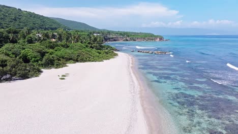 Drone-flight-over-paradise-with-sandy-beach,-clear-ocean-water-and-coral-reef-on-Dominican-Republic-at-summer-day