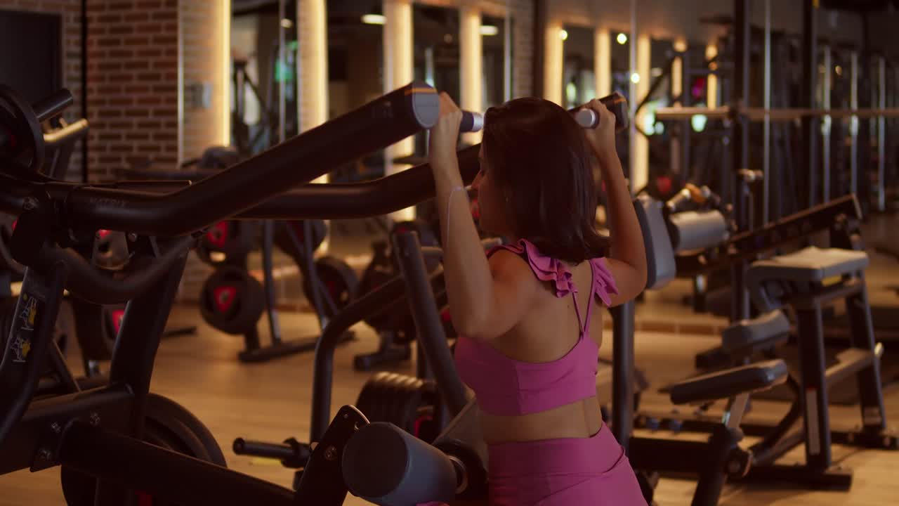 Mujer joven en el gimnasio usando una máquina de levantamiento de pesas para los músculos de la espalda