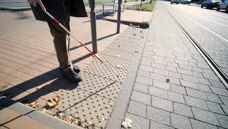 hombre con discapacidad visual cruzando la carretera con su palo con la ayuda de la acera táctil para peatones para discapacitados visuales en la ciudad.