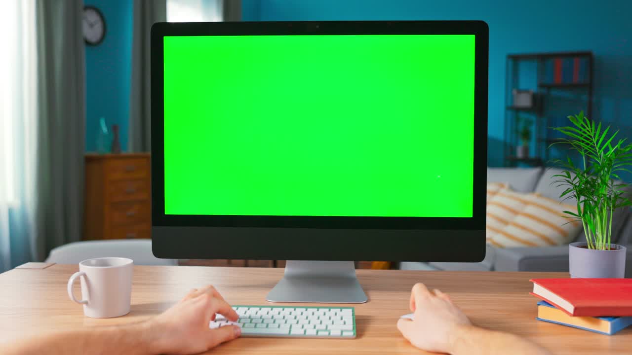 scatto di mani maschili che scrivono su una tastiera di computer con schermo vuoto. moderno personal computer con mock-up green screen display in piedi sulla scrivania della casa accogliente