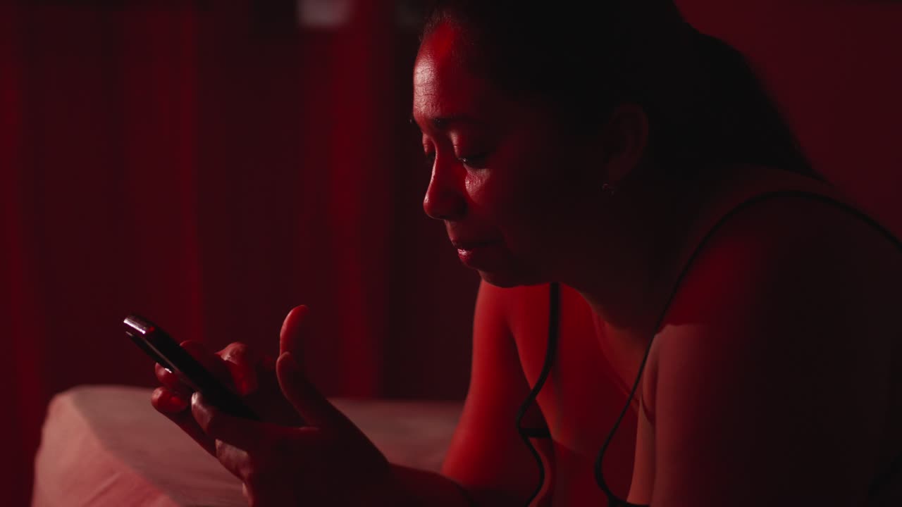 Adult Hispanic woman smiling and looking at mobile phone in a dark room