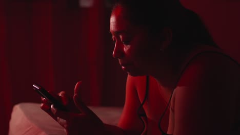 Adult-Hispanic-woman-smiling-and-looking-at-mobile-phone-in-a-dark-room