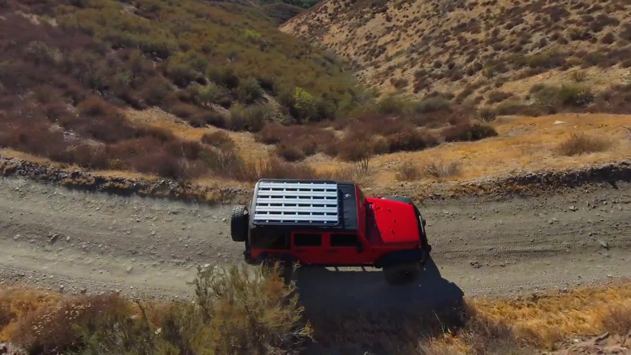 Dynaaminen ilmakuva seuraa punaista Jeep-maastoautoa sen kiitäessä ylös soraisella vuoristotiellä