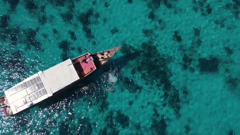 Top-Down-Aerial-View-of-People-Jumping-From-Boat-With-Solar-Panels-in-Turquoise-Tropical-Sea-Water,-High-Angle-Drone-Shot