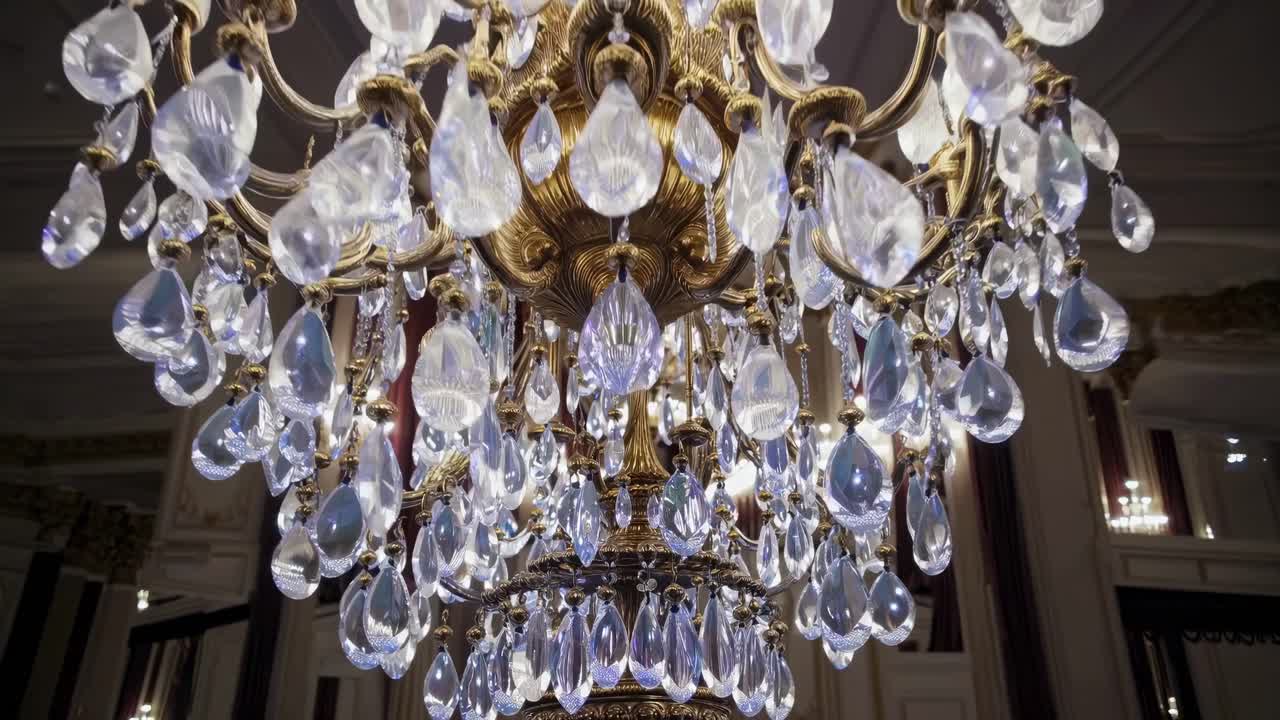 Un primo piano video, con un'angolazione dal basso, di un lussuoso lampadario, che mostra scintillanti gocce di cristallo