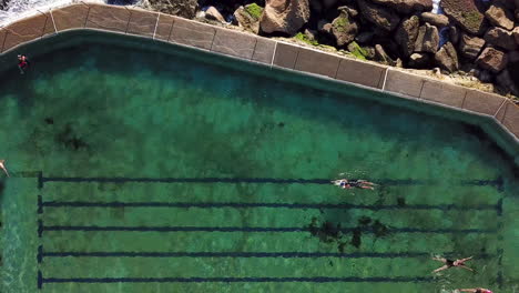 close up aerial footage of bronte sea baths top down following swimmers in beautiful crystal clear turquoise sea water