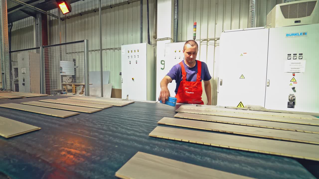 A young carpenter checks the quality of the boards. Manufacture of parquet boards.