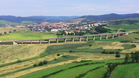 Drone-shot-of-European-route-E50-highway-road-through-green-agricultural-fields-landscape-connecting-European-continent,-Levoca-town-in-background