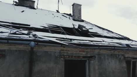 a drone ascending over a damaged and abandoned building with a partially collapsed roof covered in snow