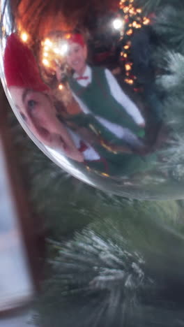 funny girl elf in a red hat looks in a new year s ball playing with its reflection. residence of santa claus. vertical video