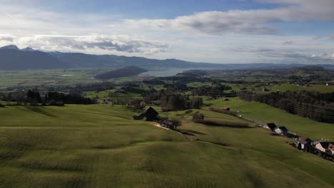 establishing cinematic aerial of open fields with beautiful lake and mountains in background