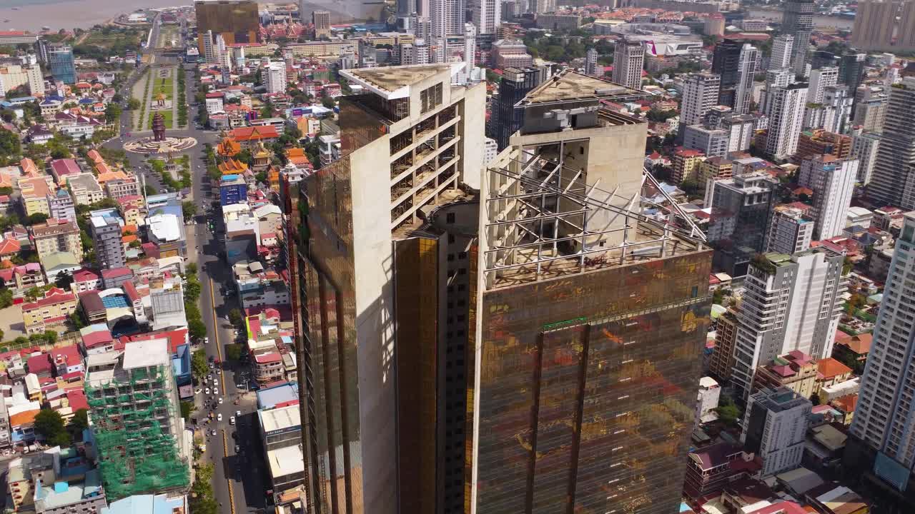 Drone circles around under construction of twin tower skyscraper Gold Tower 42 surrounding highrise commercial, residential buildings on Preah Sihanouk Boulevard with Independence Monument in view