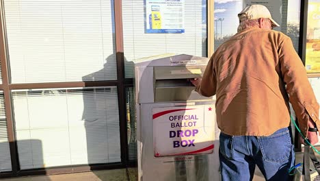 el hombre de la generación del baby boom vota dejando caer la carta de voto por correo en la ranura de la cabina de votación con el cartel de votación oficial para la elección del gobierno democrático en la carrera presidencial
